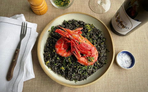 Squid ink risotto topped with vivid red Carabineros prawns, parsley and lemon zest